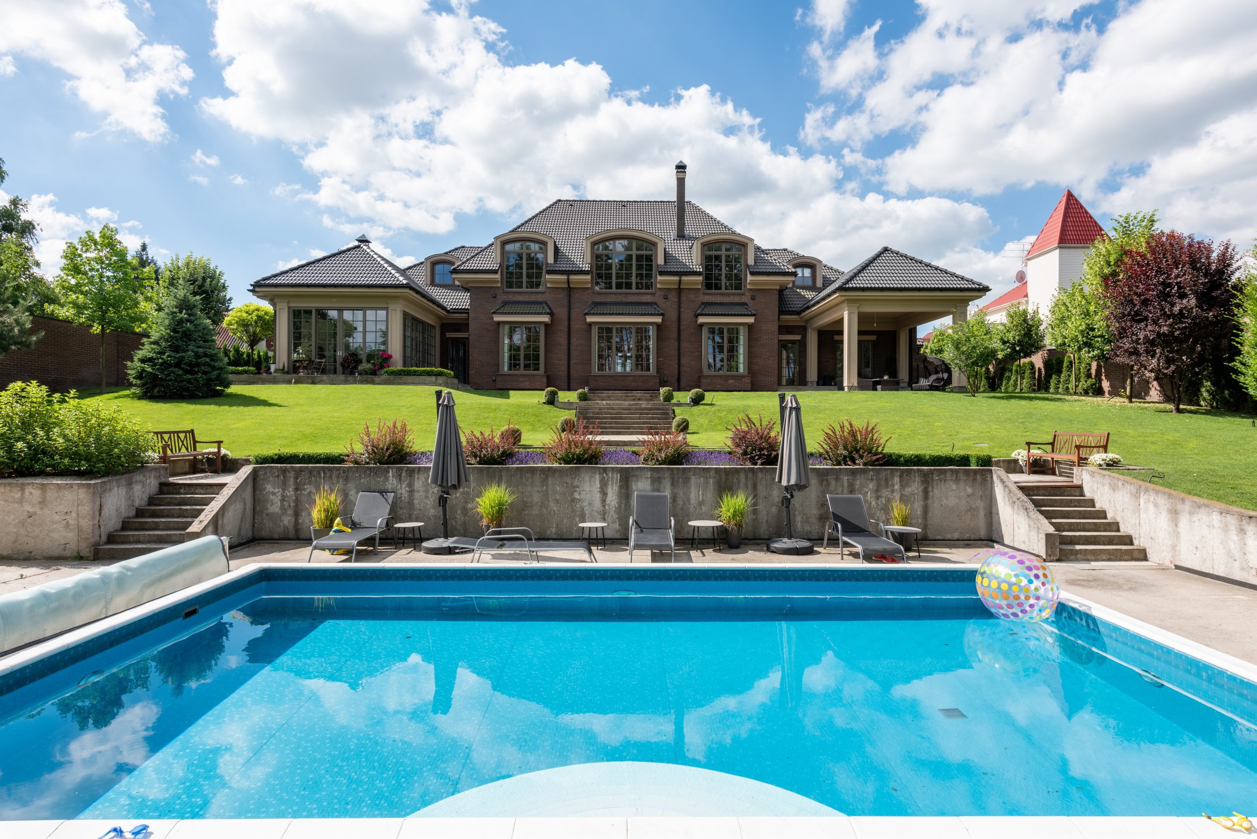 Grande maison de couleur marron avec piscine au devant avec parasol et transat